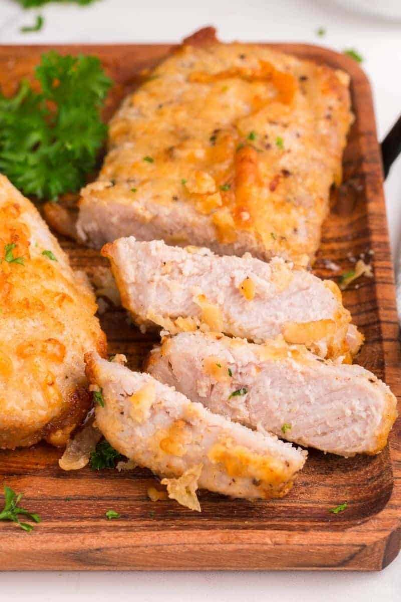 Air fryer pork chops with a Parmesan crust, sliced and served on a wooden board garnished with parsley.