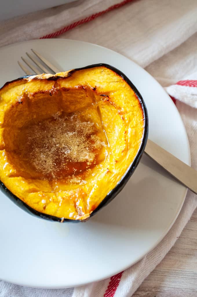 A serving of roasted acorn squash on a plate with a fork and a napkin.