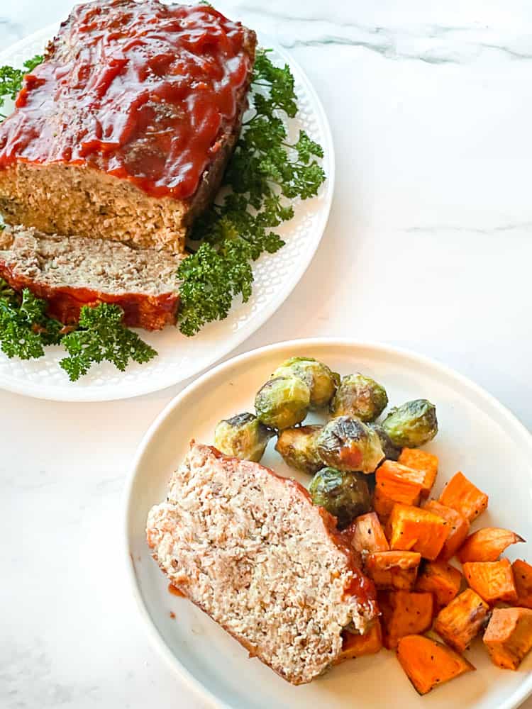 Easy Meatloaf on a platter and served up on a plate with sprouts and sweet potatoes.