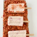 Strawberry ice cream bars being rolled in crispy topping.
