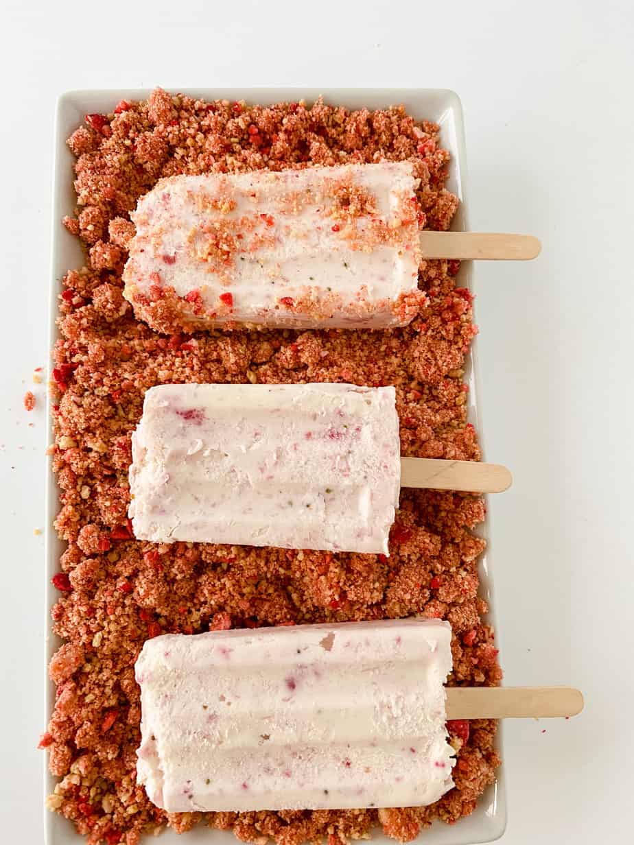 Strawberry ice cream bars being rolled in crispy topping.