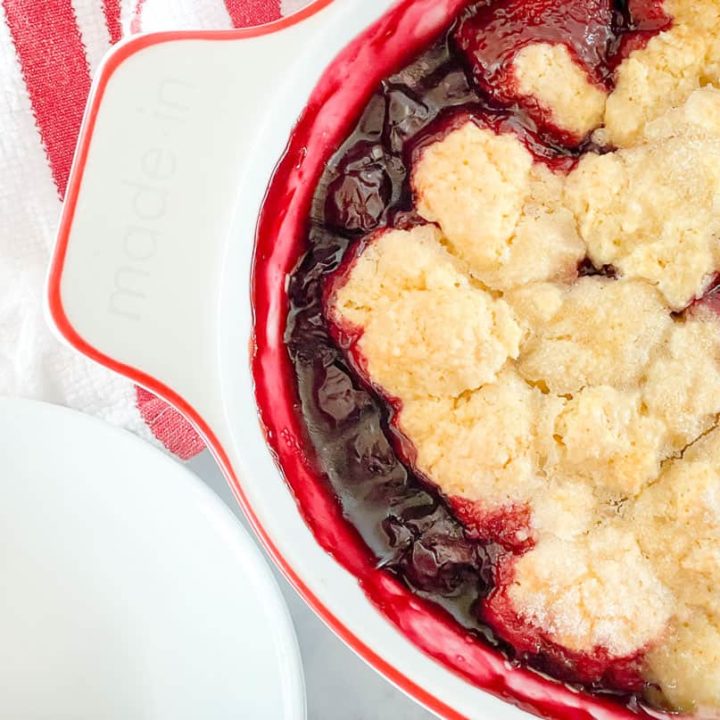 Cherry cobbler in a baking dish with plates.