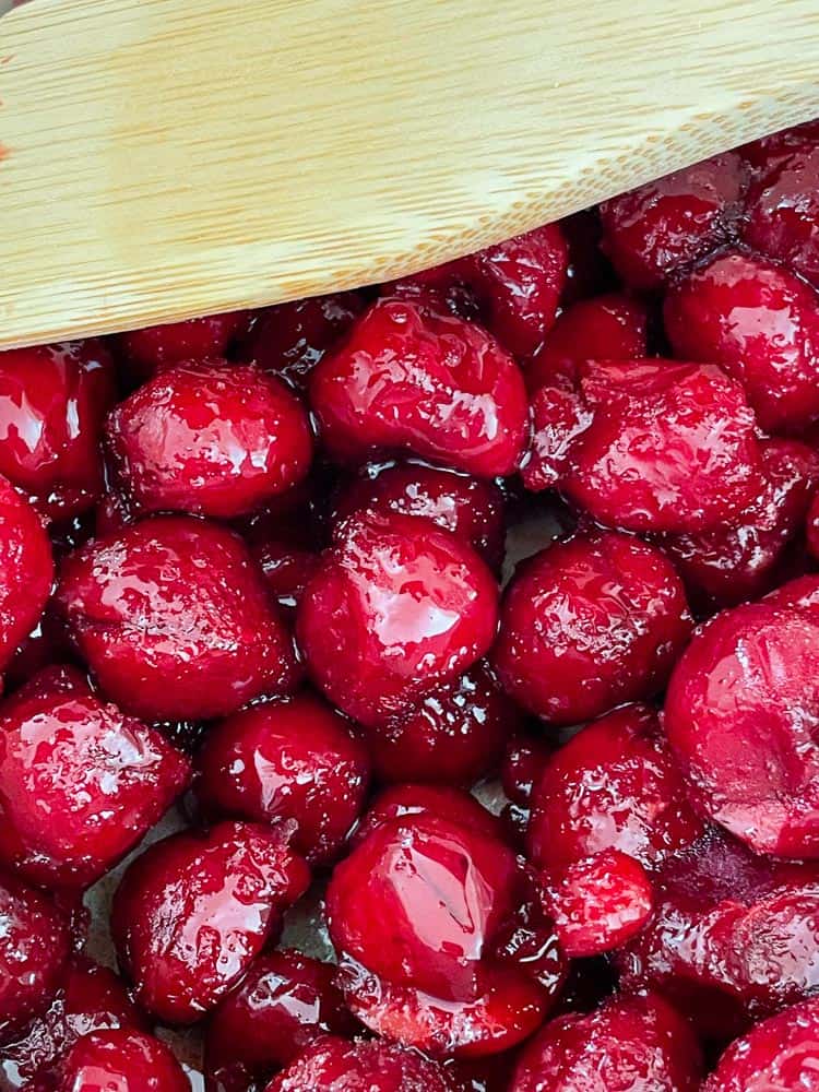 Frozen cherries with a wooden spoon in a pan.
