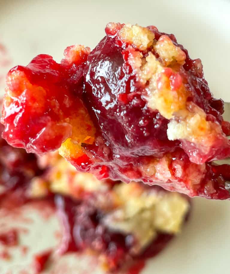 One bite of cherry dump cake on a fork with a nice cherry in the bite. Over a plate with more cake on it.