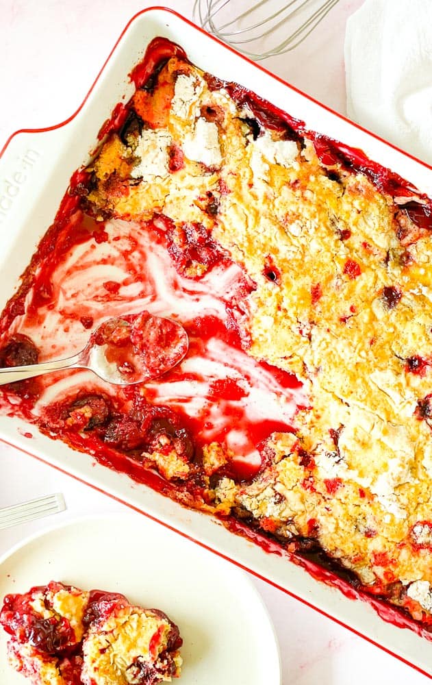 Cherry dump cake in 9x13 pan with several scoops out of it and one plate with cake on it.