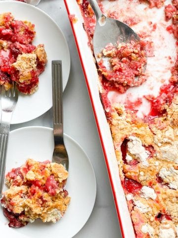 2 servings of strawberry dump cake on plates with the cake pan next to them.