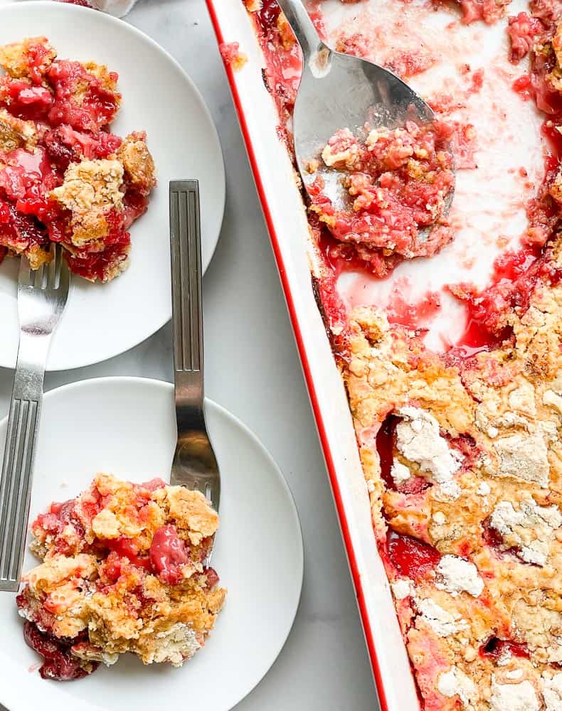 2 servings of strawberry dump cake on plates with the cake pan next to them.