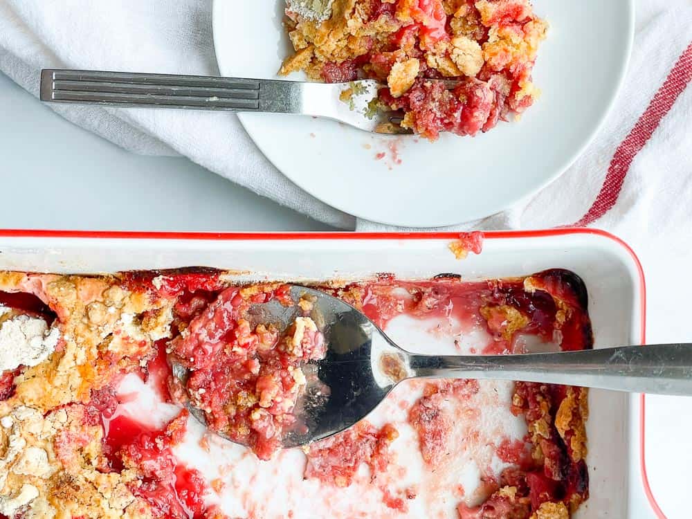 One plate of strawberry dump cake on a plate with the cake pan next to it. 