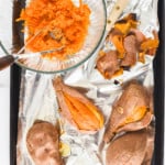 Baked sweet potatoes on a foil-lined baking tray and mashed sweet potatoes in a bowl.