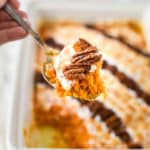 A scoop of sweet potato casserole over the rest of the casserole with pecans and marshmallows.