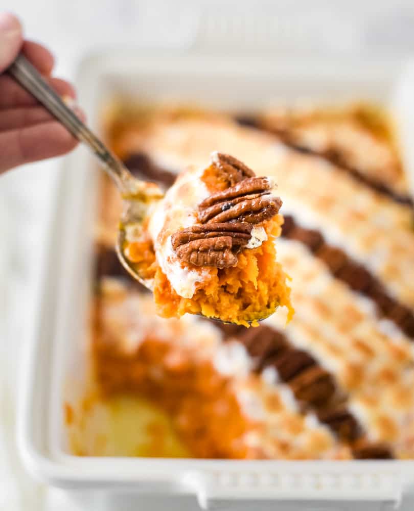 A scoop of sweet potato casserole over the rest of the casserole with pecans and marshmallows.