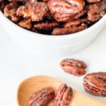 Easy Candied pecans in a bowl with a spoon and few loose pecans.