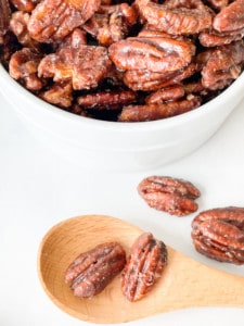 Easy Candied pecans in a bowl with a spoon and few loose pecans.