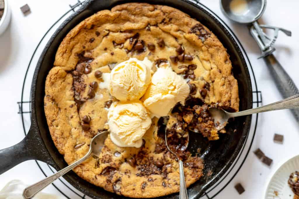 Close-up photo of chocolate chip pizookie in a skillet, topped with melting scoops of vanilla ice cream.
