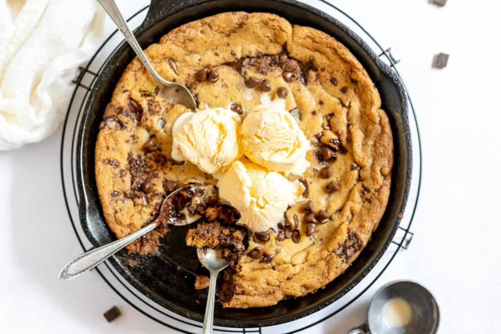 A freshly baked chocolate chip pizookie in a skillet, topped with melting scoops of vanilla ice cream.