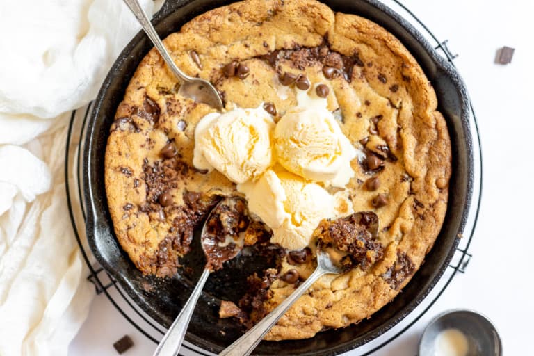 Close-up photo of freshly baked chocolate chip pizookie in a skillet, topped with melting scoops of vanilla ice cream.