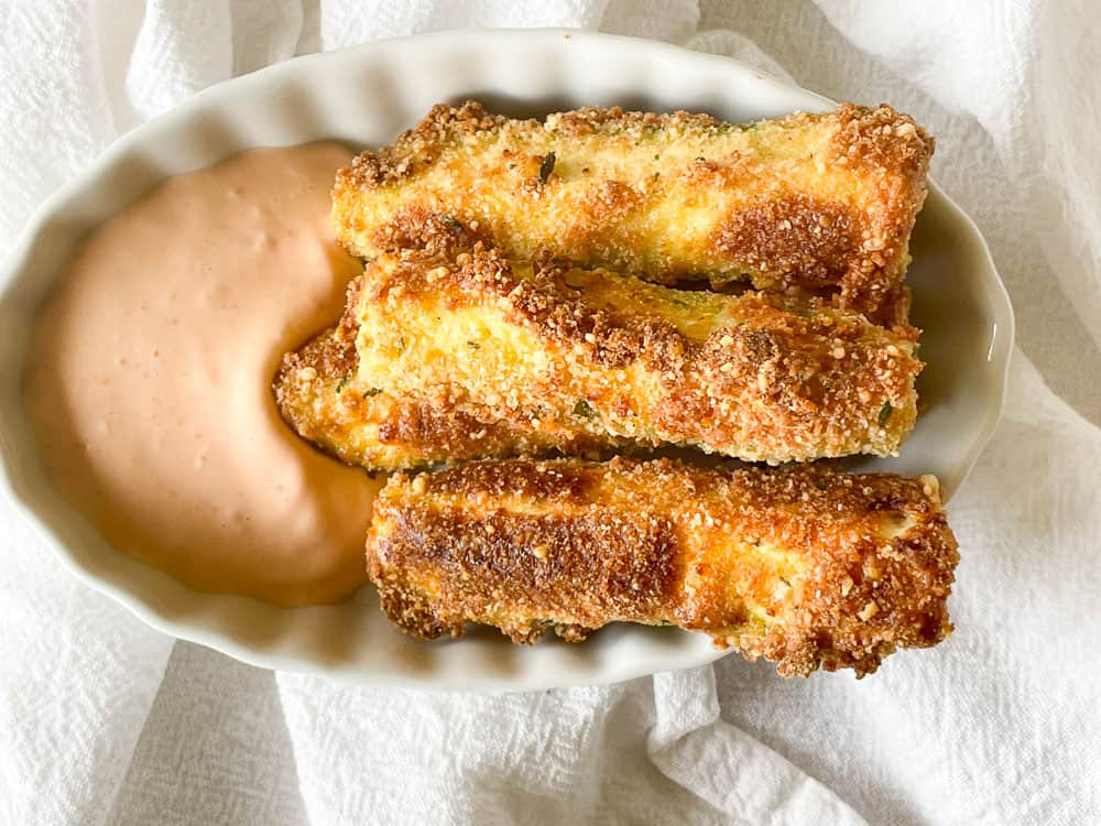 Golden-brown zucchini fries next to a dipping sauce.