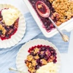 Blueberry crisp baked in a white dish, with plates of blueberry crisps topped with ice cream.