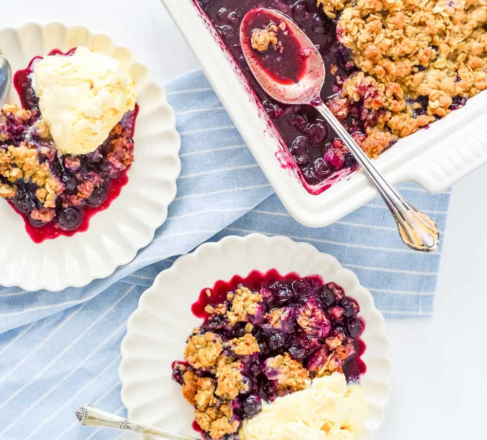 Blueberry crisp baked in a white dish, with plates of blueberry crisps topped with ice cream.