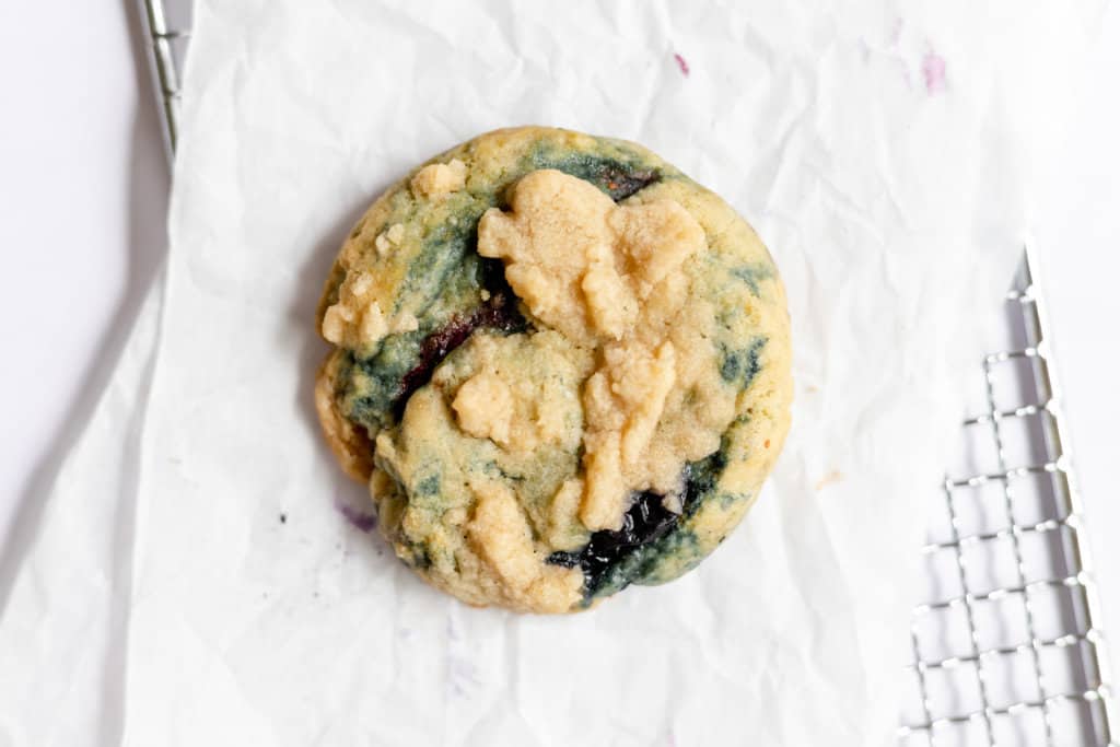 A single perfect blueberry muffin cookie on parchment and a baking rack 