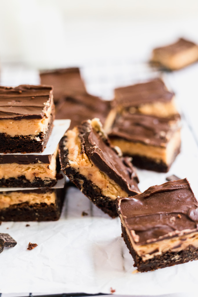 Several Buckeye Brownies, featuring rich chocolate and peanut butter layers, are arranged on a piece of parchment paper, with some bars stacked and others scattered around.