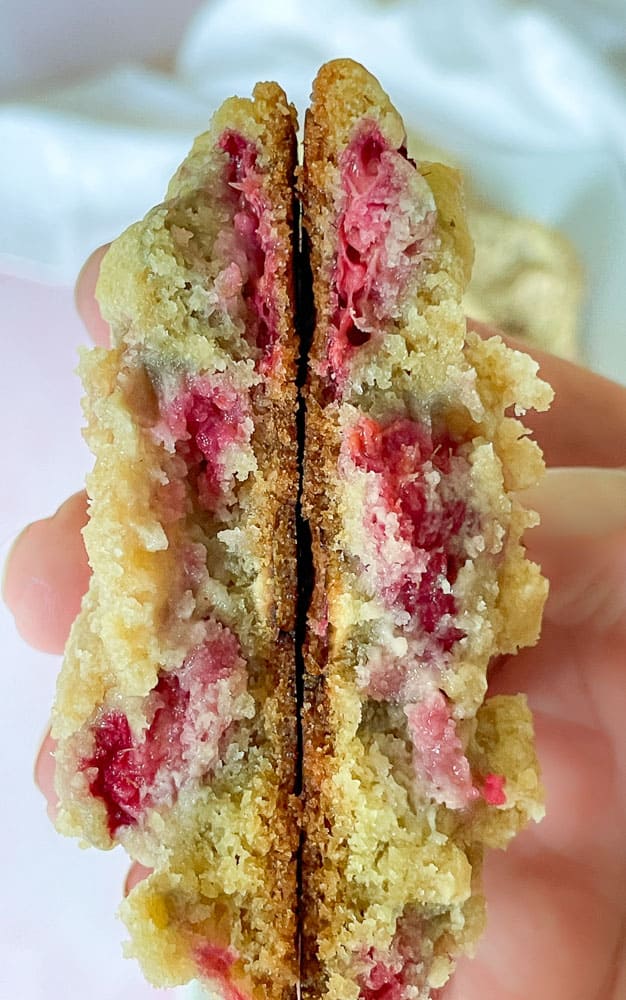 White chocolate chip cookie with raspberries broken in half to show the inside.