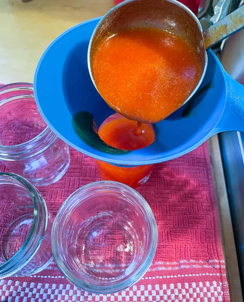 Pouring sriracha into hot sterilized jars for hot water canning.