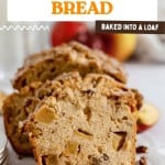 Sliced loaf of Dutch Apple Bread with visible apple chunks, pecans, and apple slices in the background on a white surface.