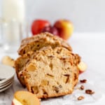 Sliced Dutch apple bread with fresh apples and pecans in the background.