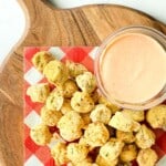 Cutting board with fried okra and dipping sauce on a checkered napkin.