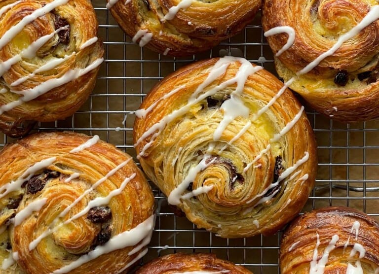 Pain aux raisins in a cooling rack drizzled with icing.