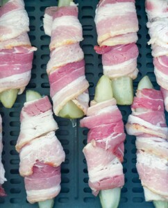 Air Fryer basket full of pickle spears wrapped in bacon.