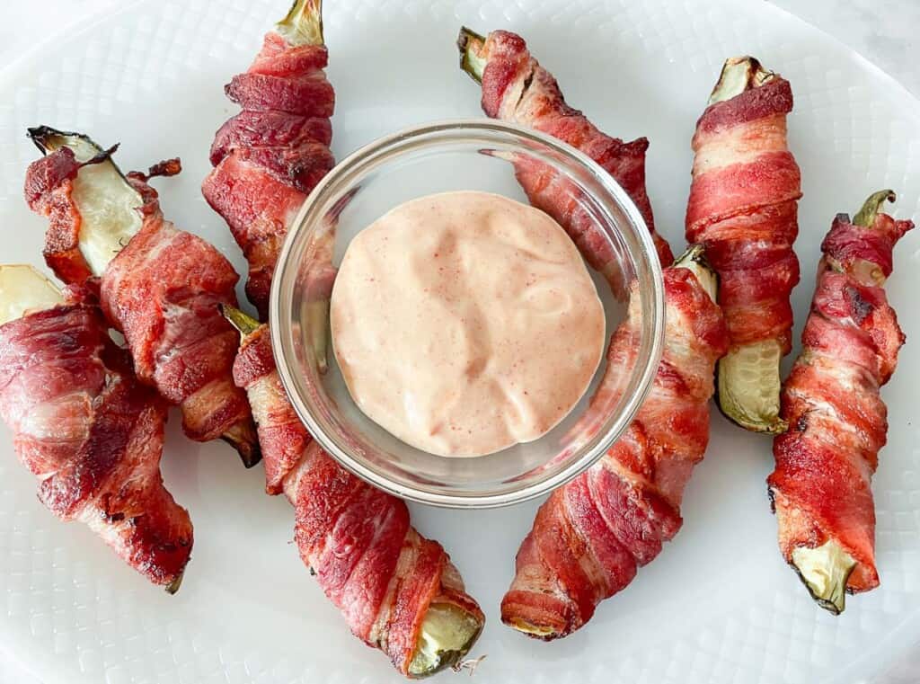 Bacon wrapped pickles on a platter with dipping sauce.