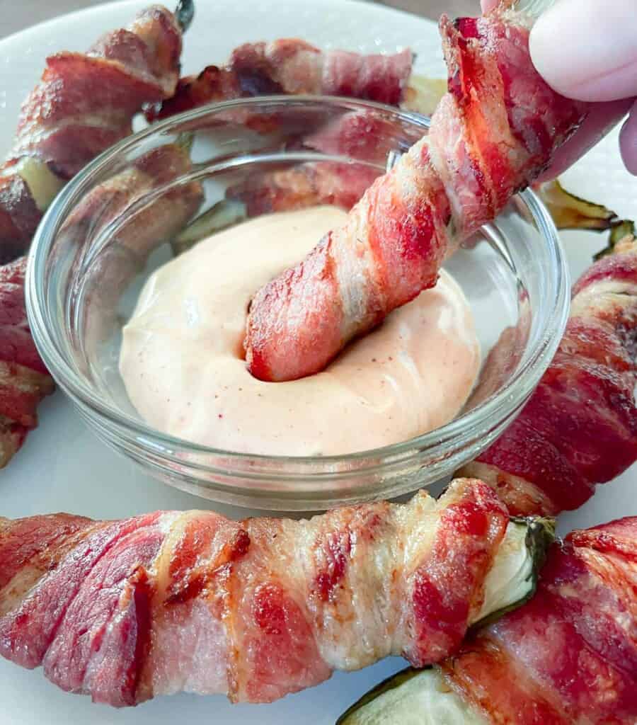 Dipping a bacon wrapped pickle in a dipping sauce.