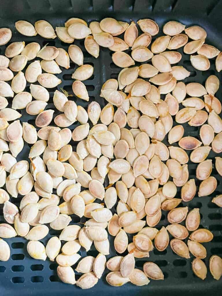 Air fryer basket with a single layer of pumpkin seeds. 