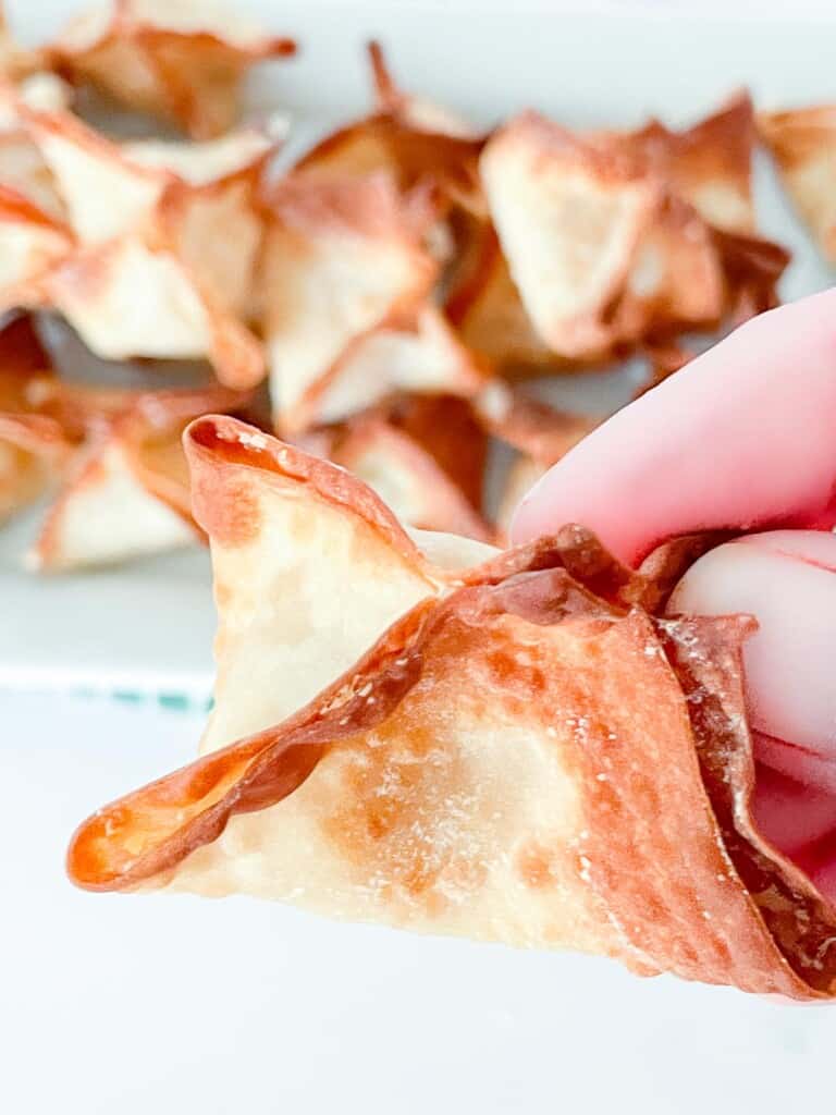 A crab rangoon up close and personal, with a platter of them in the background.