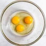 Three raw eggs in a clear glass mixing bowl for a Bourbon Pecan Pie.