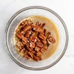 Pecans for a Bourbon Pecan Pie mixed into melted butter in a glass bowl.