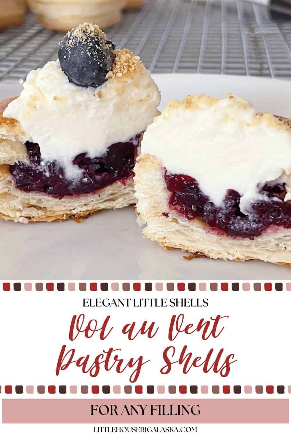 Two Vol Au Vent pastry shells filled with cherry filling and cream, garnished with a blueberry, are displayed on a white surface with a cooling rack in the background.
