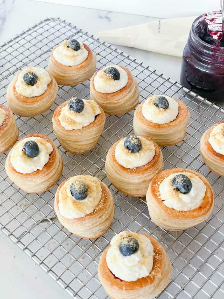 A cooling rack full of vol au vents filled with blueberry filling.