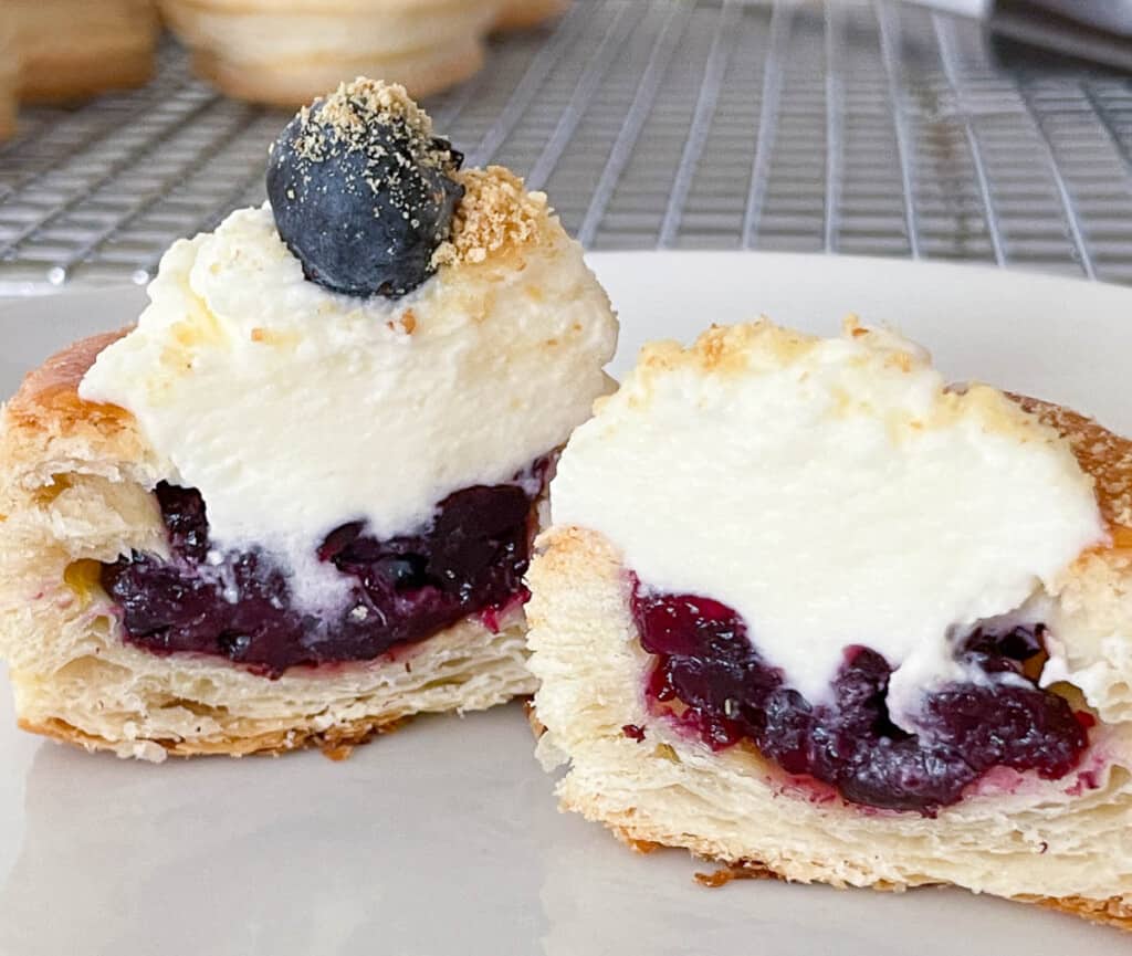 a sweet pastry case with blueberry jam, whipped cream, and a blueberry cut in half.