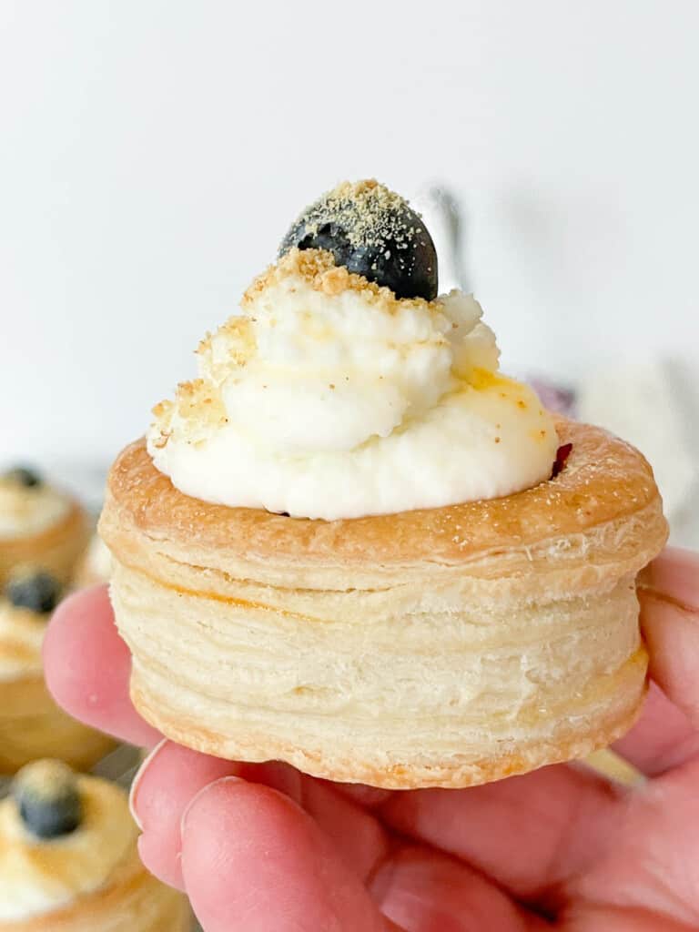 Finished vol au vent shell with a sweet filling, whipped cream, and a blueberry on top.
