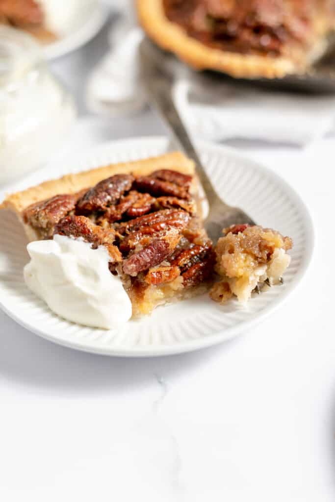 Pecan pie with a bite on a fork with whipping cream on the plate.
