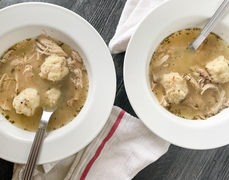 White bowls of chicken and dumplings with spoons and linens.