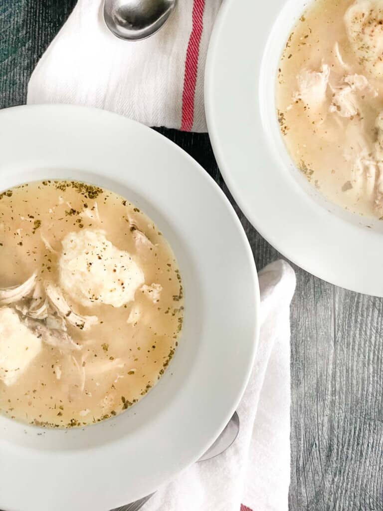 2 bowls of chicken and dumpling soup with spoons and linens.