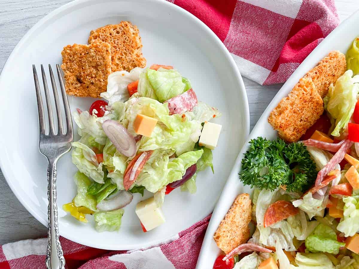 A plate of antipasto salad with a fork next to a napkin and the salad platter.