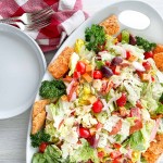 Salad on a platter with two plates, two forks, and two napkins.