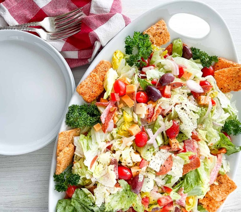 Salad on a platter with two plates, two forks, and two napkins.