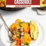 A serving of Chicken Fajita Casserole with melted cheese, bell peppers, and herbs on a white plate, garnished with avocado slices and served alongside a fork.