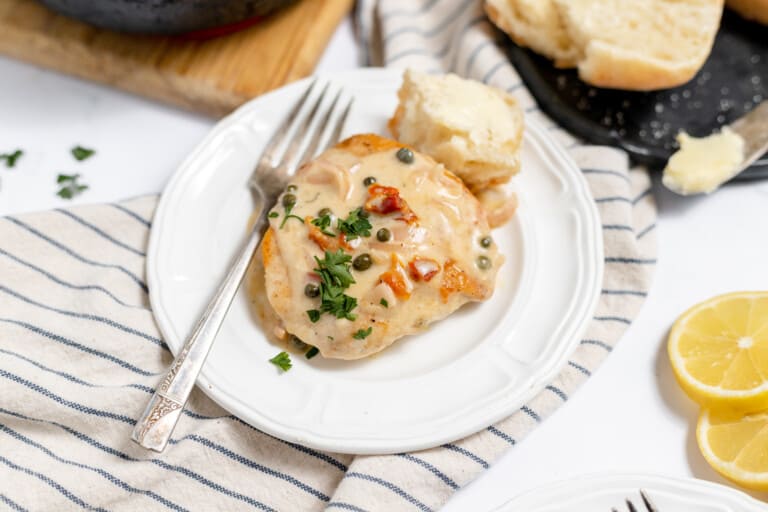 Chicken with a lemon butter sauce on a plate with crusty bread.